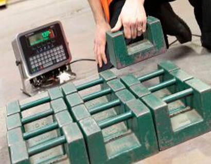 Technician calibrating a digital scale with cast iron weights for precise force measurement.